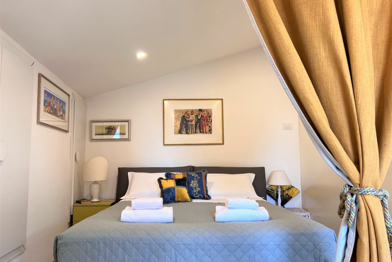 Una cama bien hecha con dos almohadas, una mesita de noche con una lámpara y un cuadro en la pared.