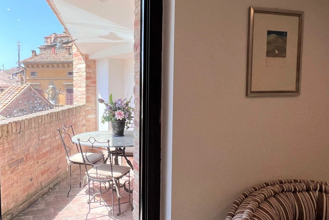 A balcony with a table and chairs, a potted plant, and a framed picture on the wall.