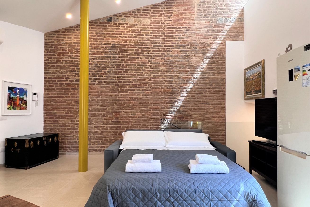 Quarto de hotel com parede de tijolos, cama com colcha azul, almofadas brancas e toalhas.