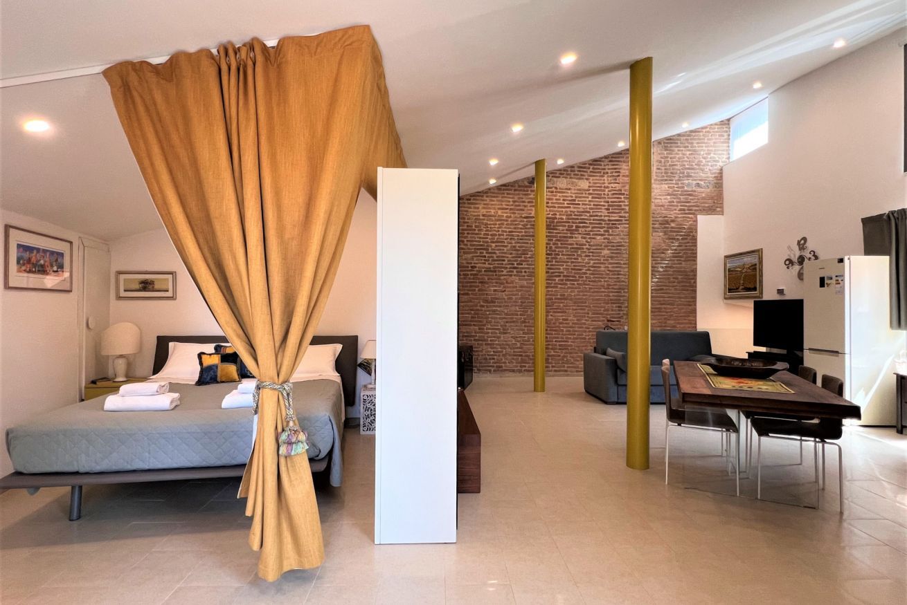 Een moderne hotelkamer met een bed, een witte kolom, een zithoek en een metselwerk muur.