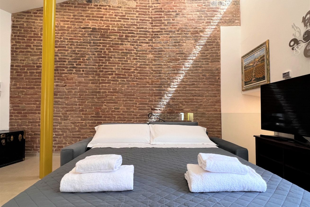 Een hotelkamer met een bakstenen muur, een bed met witte lakens, een televisie en een gele zuil.