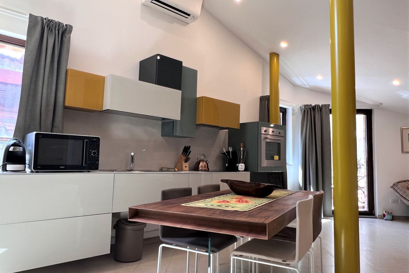 Una cocina moderna con armarios blancos, microondas y un lavamanos. Hay una mesa de comedor con sillas y un cuenco decorativo sobre la mesa.