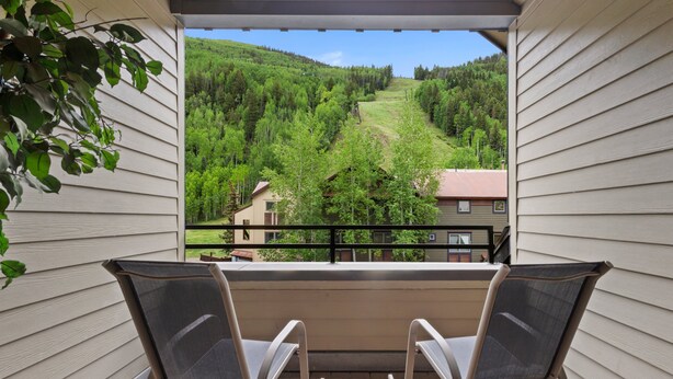 Ein Balkon mit zwei Stühlen, der auf einen schönen Ausblick über ein grünes Tal und Häuser blickt.