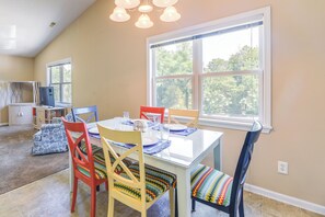 Un comedor con mesa de vidrio, sillas coloridas y un ventanal con vistas a árboles.