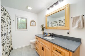 Une salle de bain avec un meuble-lavabo en bois, un grand miroir, un lavabo blanc et un rideau de douche orné d’un motif naturel.
