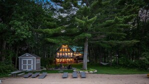 Eine Lodge mit einem großzügigen Speisesaal, einem kleinen Gästehaus und einem Strand mit Liegestühlen.