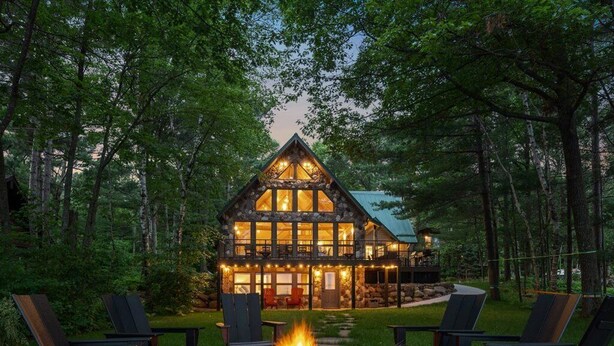 Eine Lodge mit Kamin aus Stein, umgeben von Adirondack-Stühlen, gelegen in einem bewaldeten Gebiet.