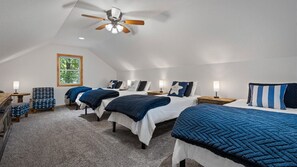 Een slaapkamer met twee bedden, een plafondventilator, een raam met uitzicht en een klein tafeltje met een lamp.