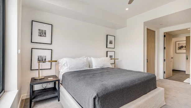 A modern bedroom with a large bed, bedside tables, framed artwork on the walls, and a ceiling fan.