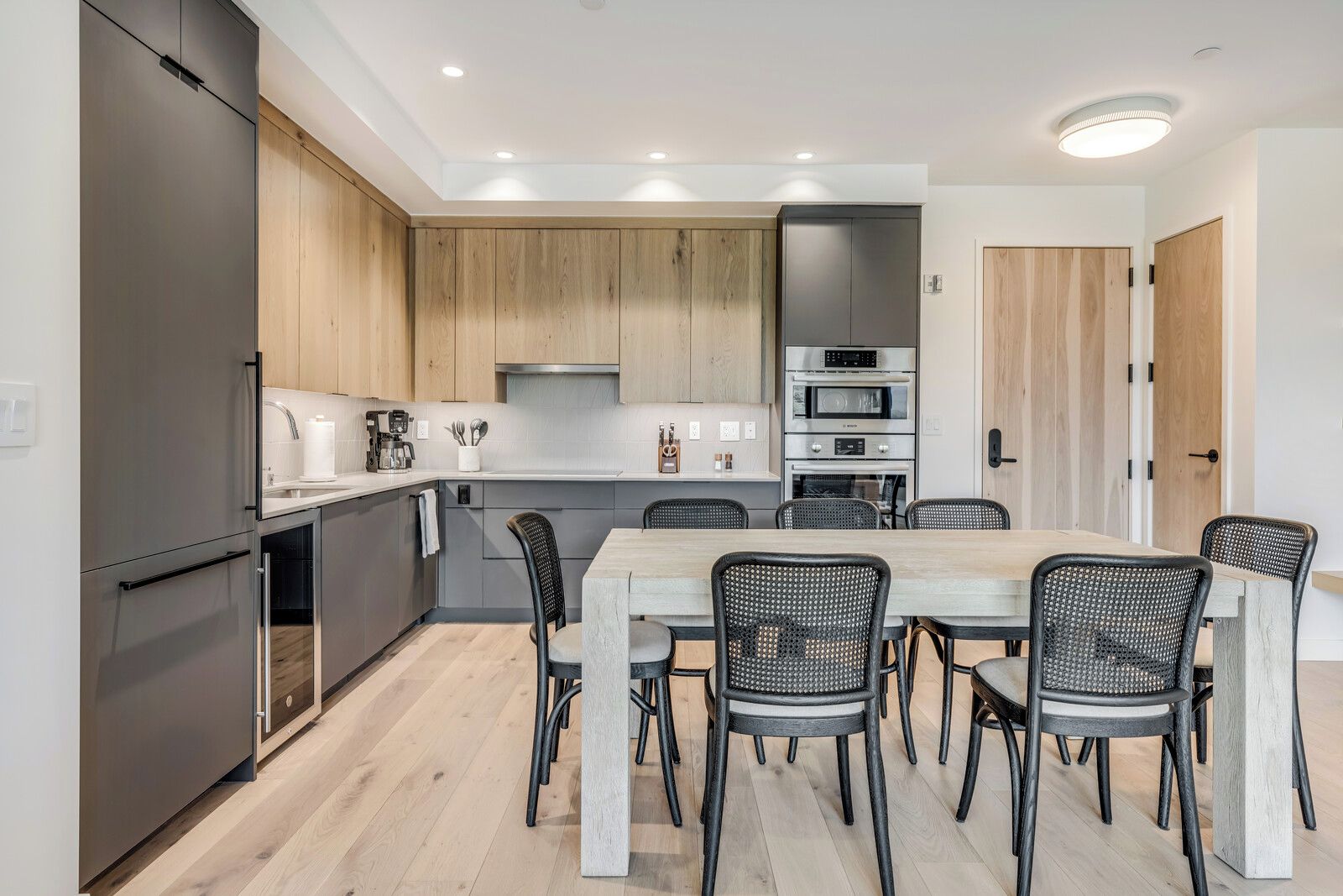 Cocina moderna con comedor, que cuenta con una isla central, electrodomésticos integrados y acabados en madera clara.