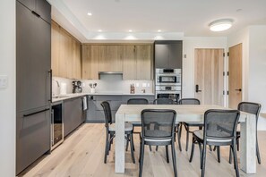 A modern kitchen with a dining area, featuring a central island, built-in appliances, and a light wood finish.
