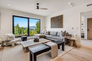 Ein modernes Wohnzimmer mit großem Fenster, einer Couch, einem Couchtisch und einem Deckenventilator.