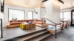 A modern living room with a sofa, ottoman, and coffee table, a staircase, and large windows.
