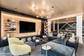 A modern living room with a large flat-screen TV, comfortable seating, and a decorative wall with a geometric light pattern.