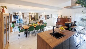 Une cuisine moderne dotée d’un îlot central, de chaises vertes et d’un coin repas agrémenté d’un lustre.