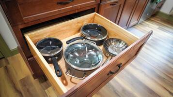 A wooden drawer with kitchenware including pots and pans.
