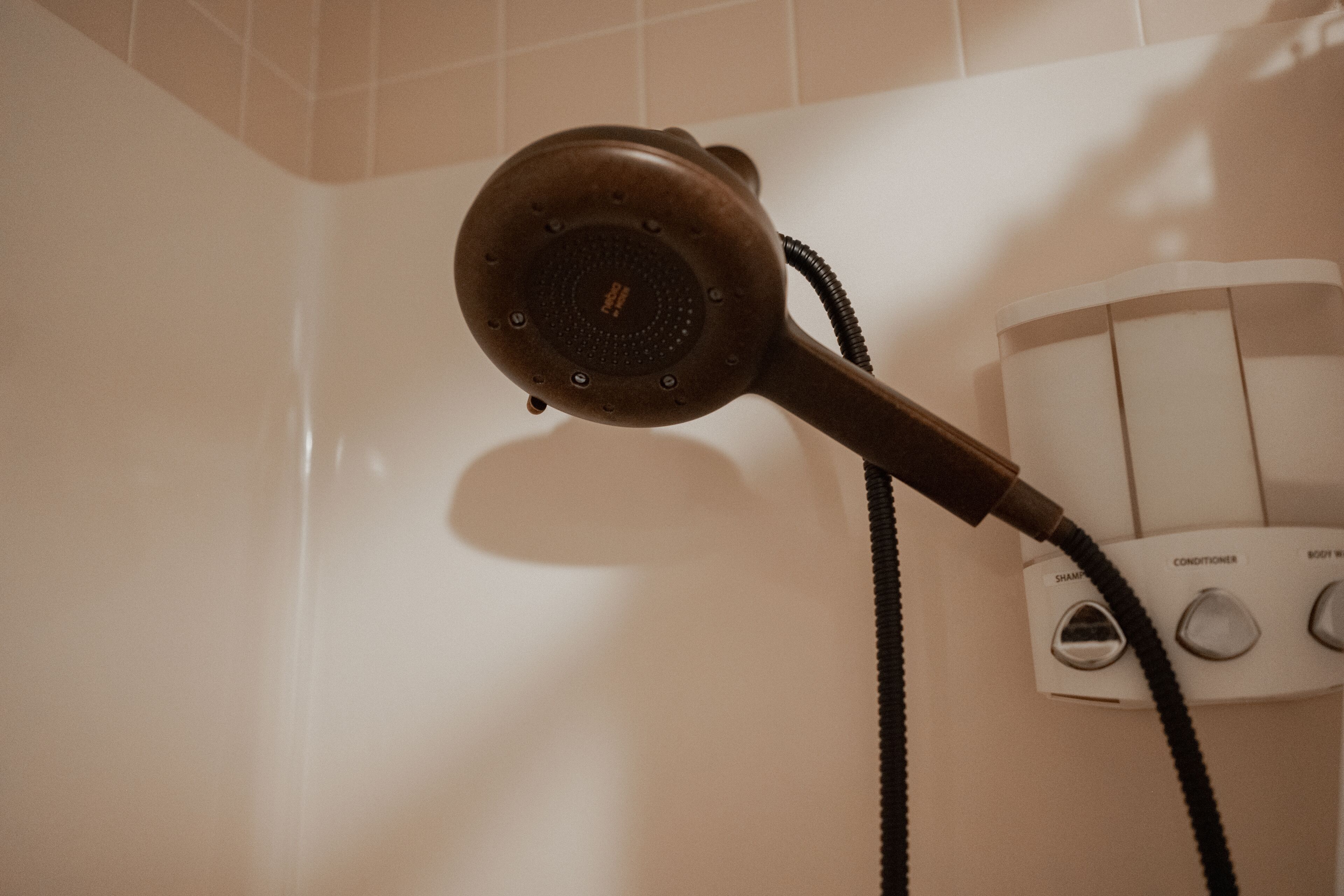 A hairdryer mounted on a wall with a control panel featuring buttons labeled "SHAMPOO," "CONDITIONER," and "BODY WASH."