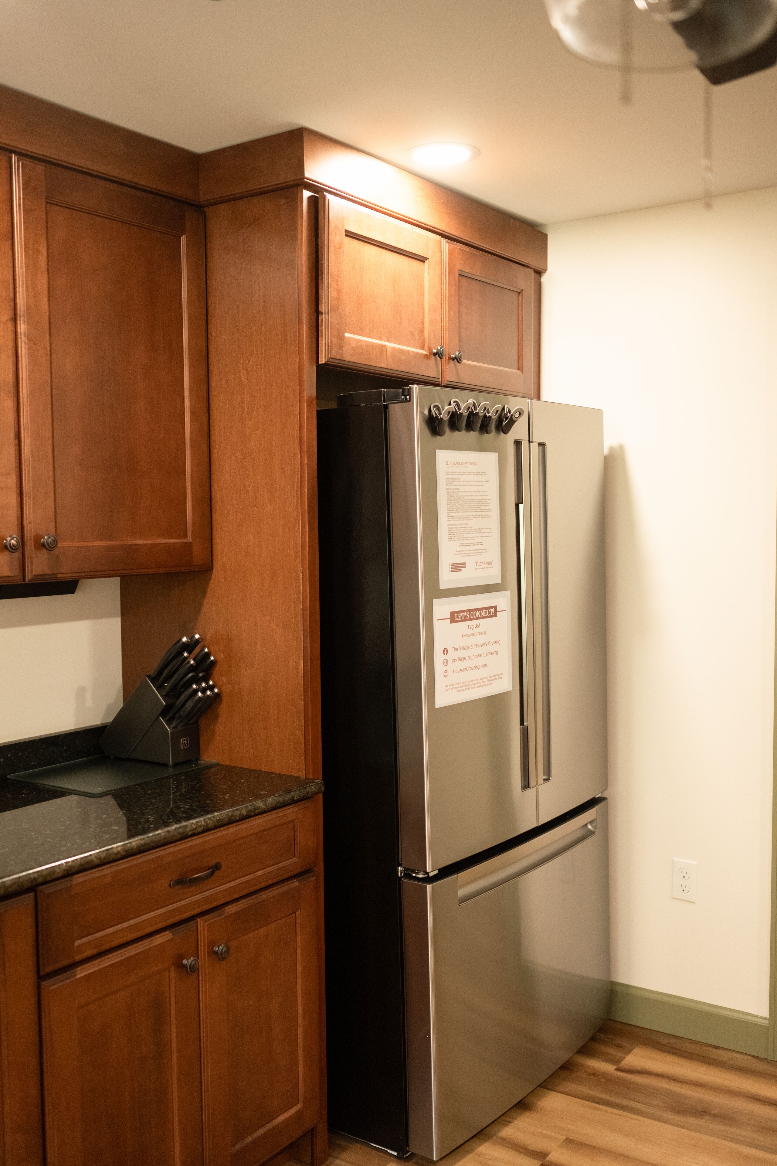 A kitchen with wooden cabinets, a stainless steel refrigerator, and a black countertop.