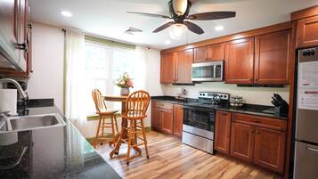 A modern kitchen with wooden cabinets, a stainless steel refrigerator, a microwave, and a stove. There is a dining area with a table and chairs.