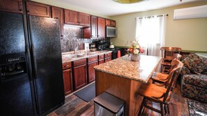 Una cocina con armarios de madera, un refrigerador negro, un microondas, un lavamanos y un comedor con sillas y una mesa.