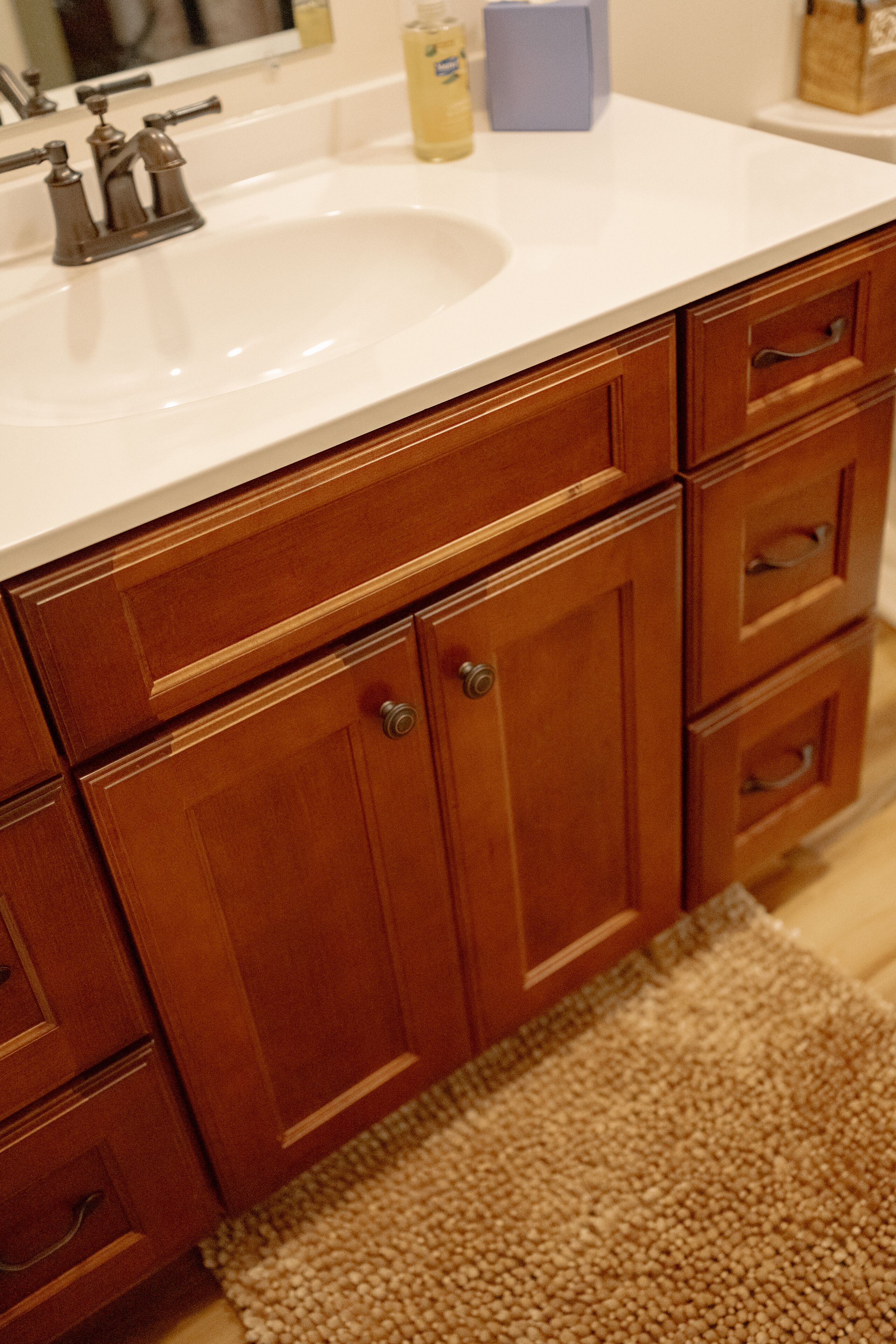 A bathroom with wooden cabinets, a white sink, and a beige rug.