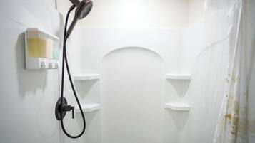 Un baño con ducha, dispensador de jabón y retrete.