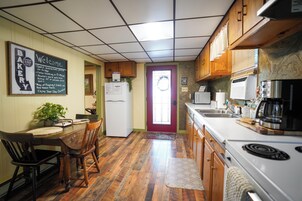 Una cocina con gabinetes de madera, un refrigerador, una estufa y un comedor con sillas y una mesa.