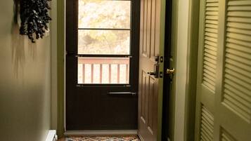 A hallway with a wooden floor, a dark door with a window, and a green door on the right.