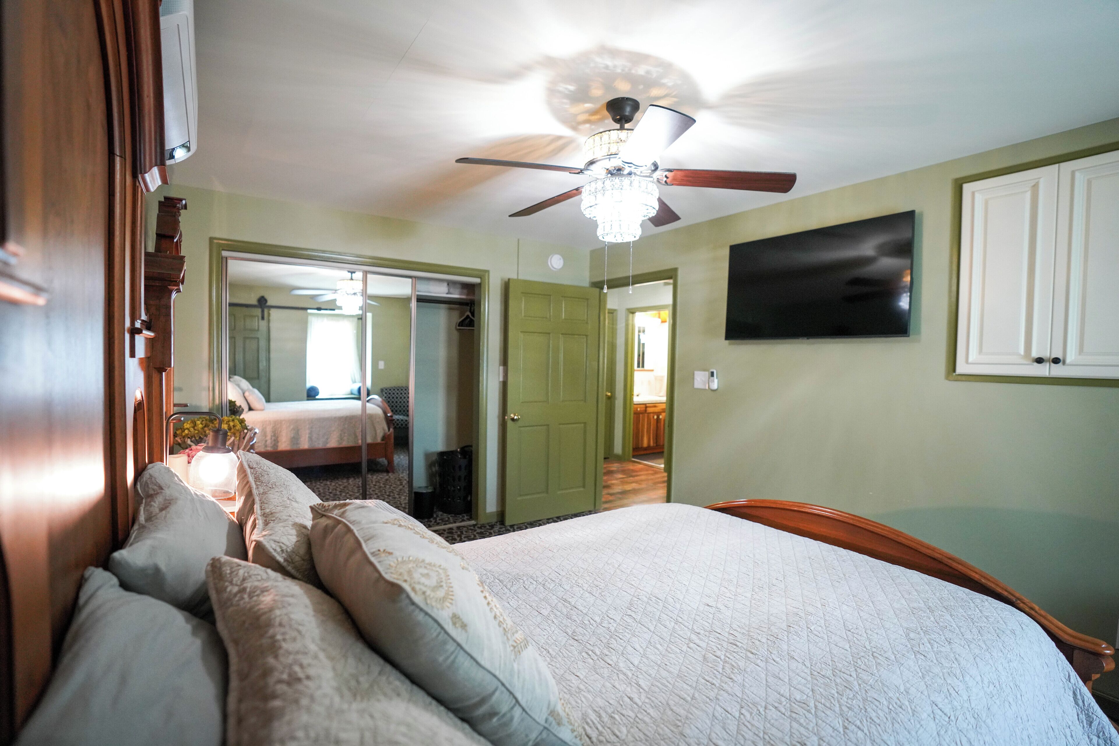 A bedroom with a bed, a ceiling fan, a television, and a green door.