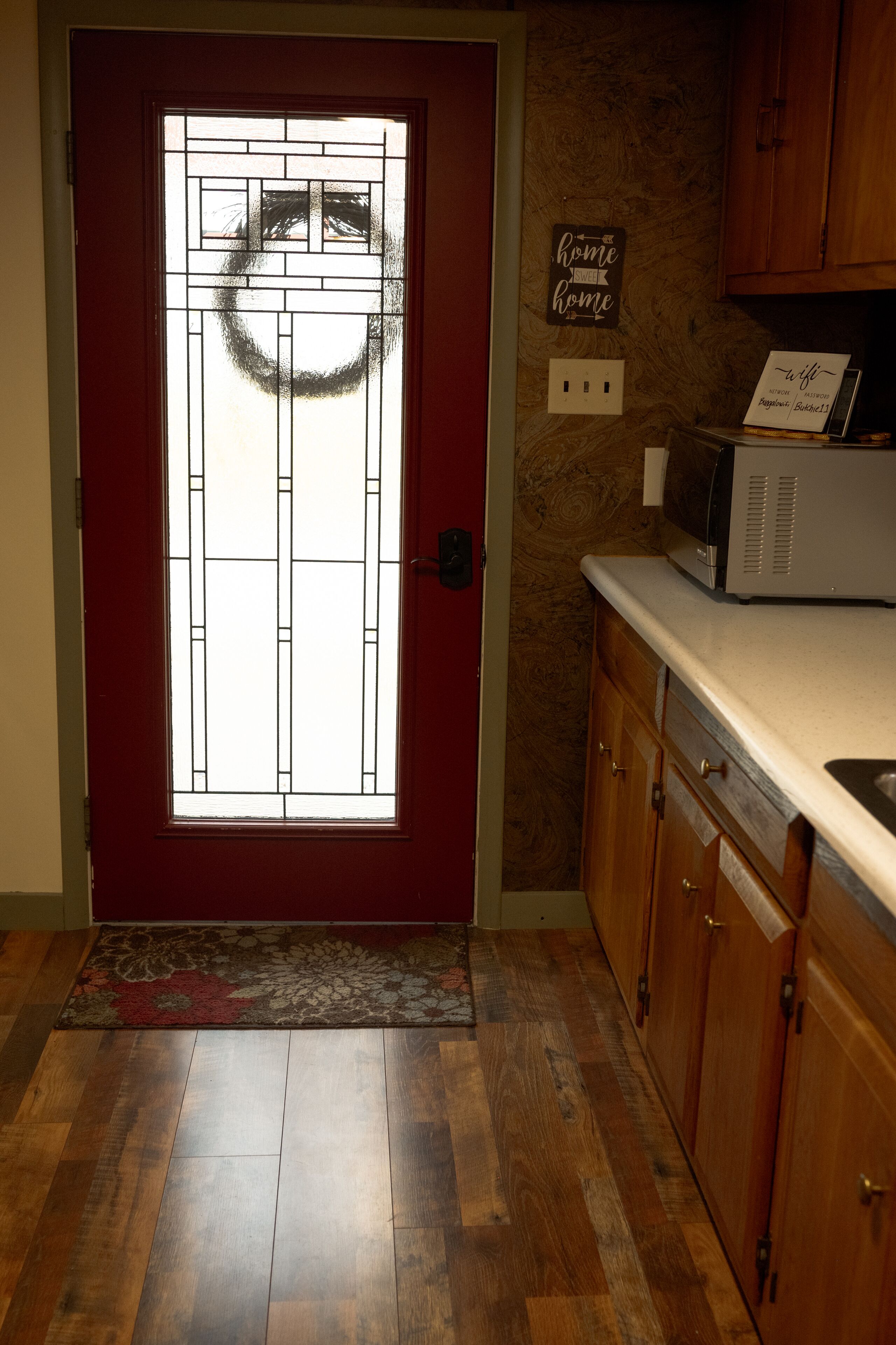 A kitchen with wooden cabinets, a microwave, and a red door with a decorative glass panel.