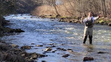A person standing in a river with rocks and trees in the background.