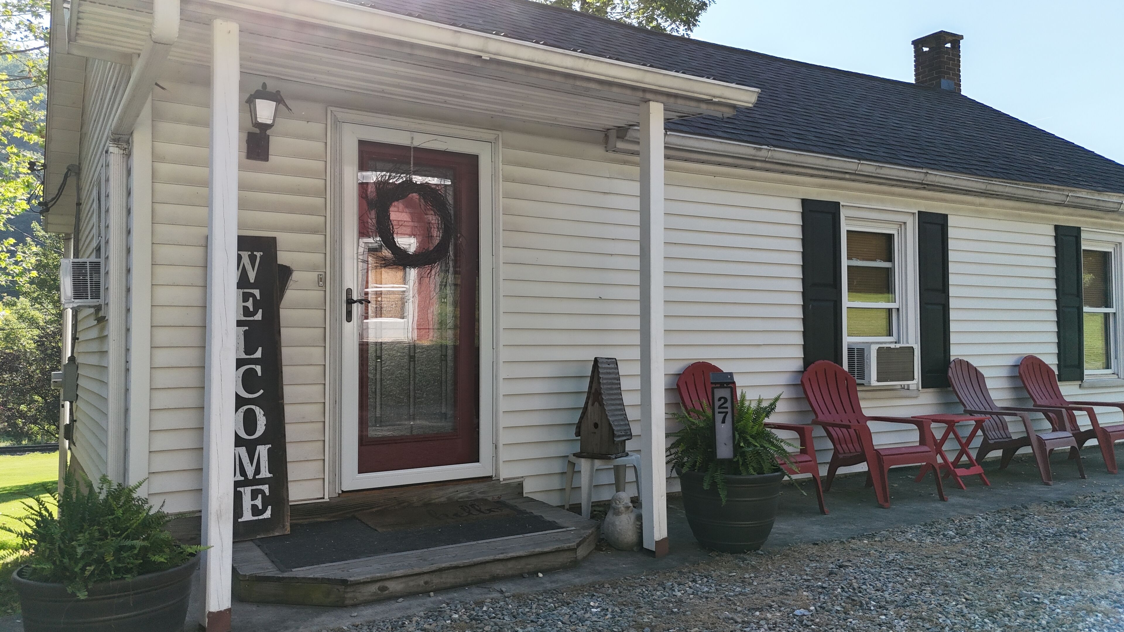 A house with a 'WELCOME' sign, a front door, and a porch with Adirondack chairs.