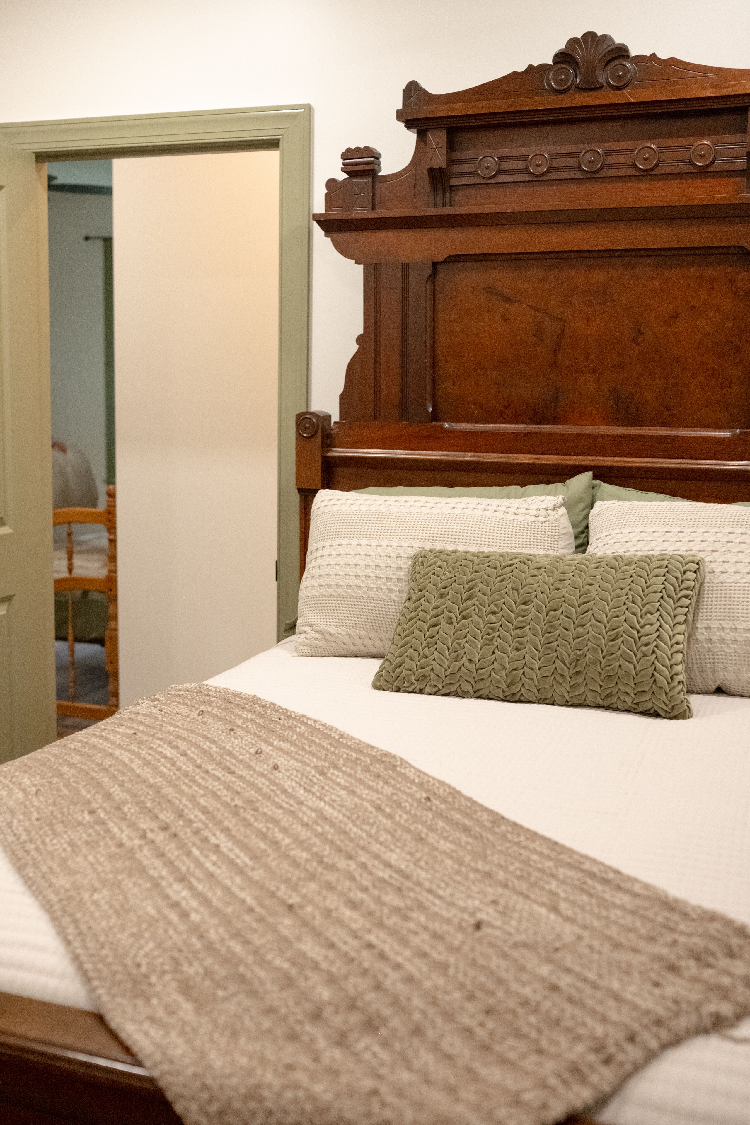 A neatly made bed with a wooden headboard, a green knitted throw, and white pillows.
