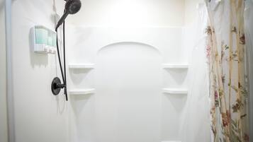 A shower area with a handheld showerhead, a soap dispenser, and a floral shower curtain.