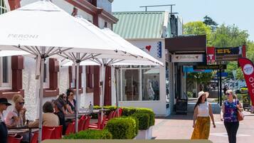 An outdoor dining area with red chairs and white umbrellas, a storefront with a sign reading "Stirling Sports," and a clear sky.