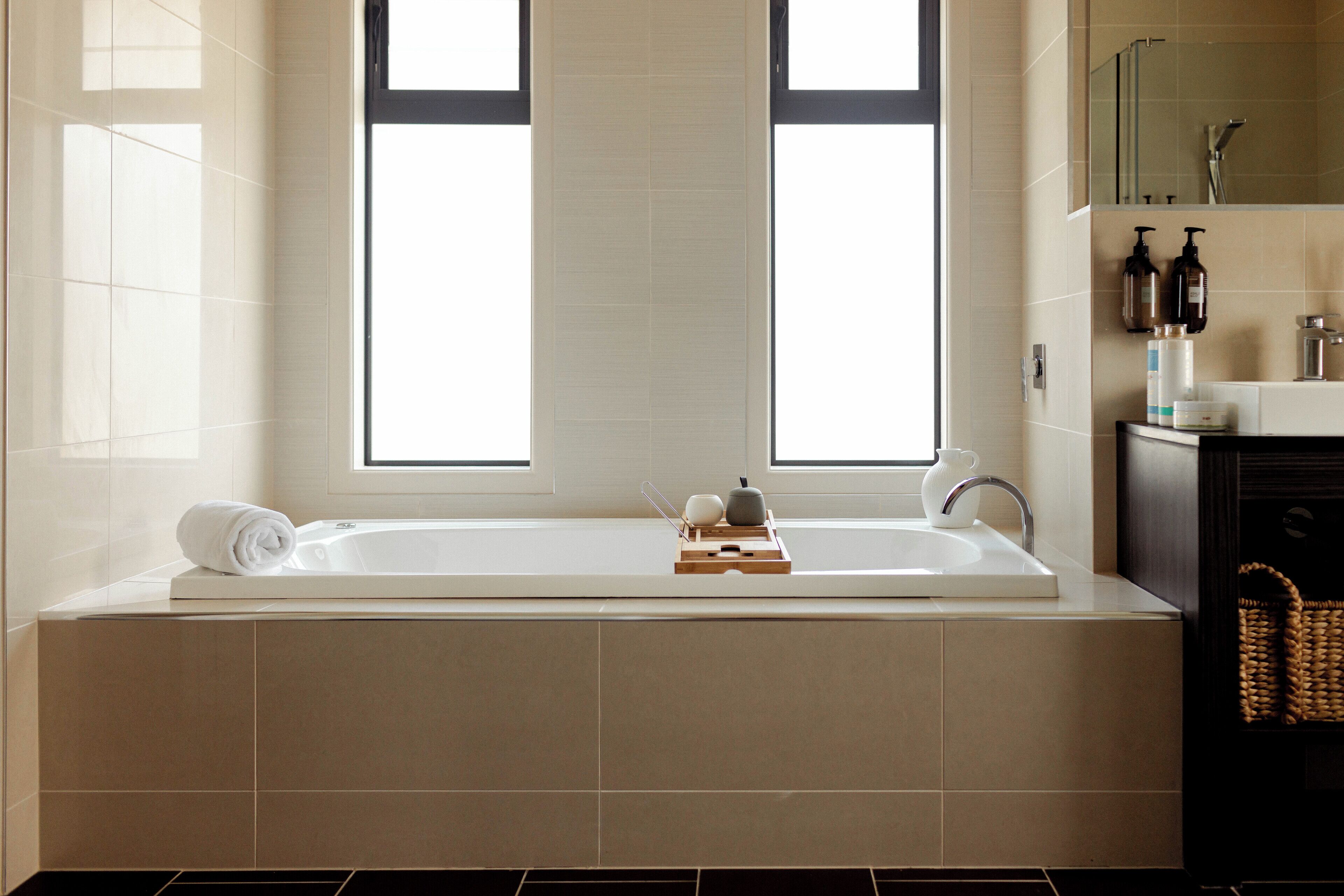 A modern bathroom with a large bathtub, a window, and a shelf with toiletries.