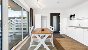 Een moderne keuken met witte kasten, een houten eettafel en uitzicht op de stad door grote ramen.