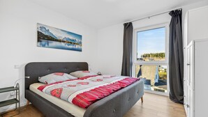 Een slaapkamer met een bed, een schilderij, een raam met gordijnen en uitzicht op een balkon.