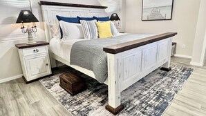 Une chambre à coucher avec un lit, des tables de chevet, une commode, un tapis et un tableau encadré au mur.