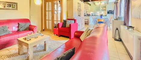 Un saló amb un sofà vermell, una taula de centre i un butac armchair vermell. Al fons, es veu una cuina amb armaris blancs i una zona de menjador.
