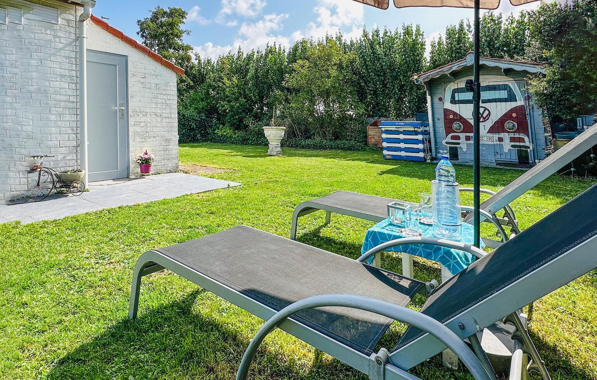 Een achtertuin met twee loungestoelen, een kleine tafel met een blauwe tafelkleed, een waterfles en een decoratieve fontein.