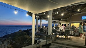 Un espace extérieur aménagé pour les repas, avec des tables et des chaises, donnant sur une étendue d’eau.
