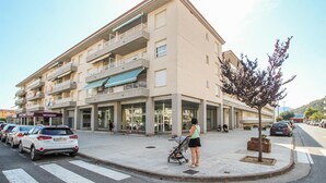 Ett hotell med flera våningar, balkonger, en restaurang och ett område för fotgängare där bilar är parkerade.