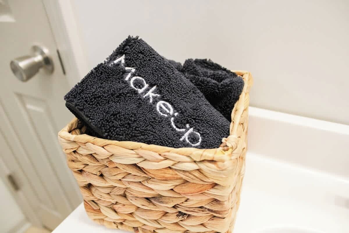 A woven basket containing black towels with the word 'makeup' embroidered on them.