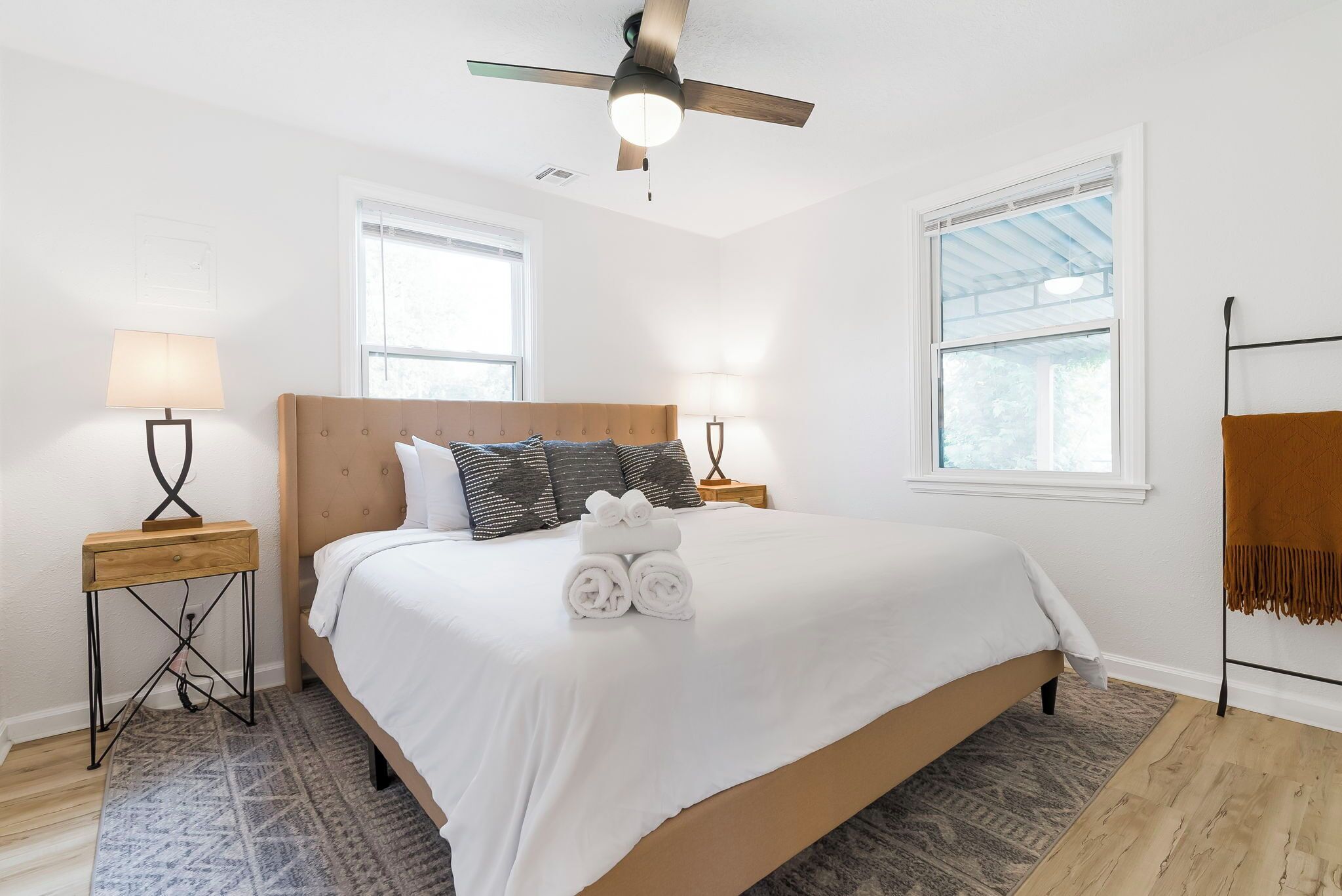 Une chambre à coucher avec un lit, deux lampes de chevet, un ventilateur de plafond, une fenêtre et un tapis à motifs.