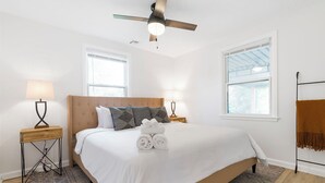 Une chambre à coucher avec un lit, deux lampes de chevet, un ventilateur de plafond, une fenêtre et un tapis à motifs.