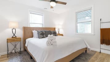 Une chambre à coucher avec un lit, deux lampes de chevet, un ventilateur de plafond, une fenêtre et un tapis à motifs.