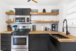 A modern kitchen with black cabinets, stainless steel appliances, wooden countertops, and white tiled backsplash.