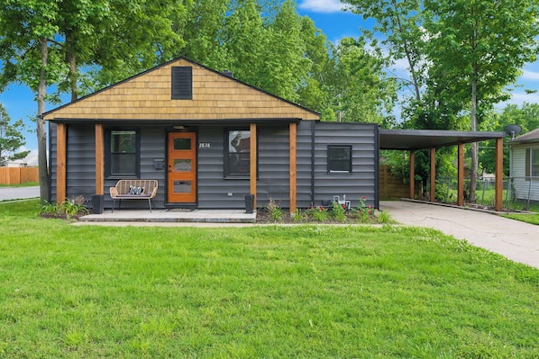 A modern single-story house with a wooden shingle roof, a front porch with a bench, and a small garden area.