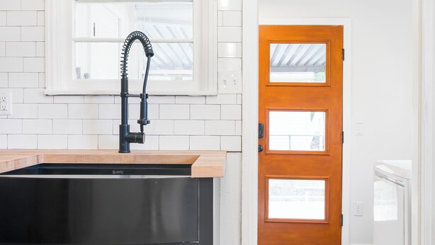 Une cuisine avec un évier noir, un dosseret de carrelage blanc et une porte en bois dotée de panneaux de verre.